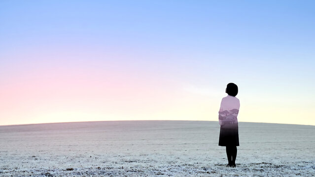Double exposure of a woman seen from behind on a snowfield blended with a pink dawn sky