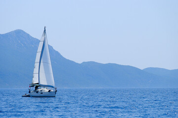Fototapeta premium A sailing yacht sailing peacefully in the distance against the Greek Ionian mountains in the background.