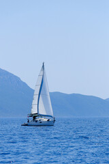 Fototapeta premium A sailing yacht sailing peacefully in the distance against the Greek Ionian mountains in the background.