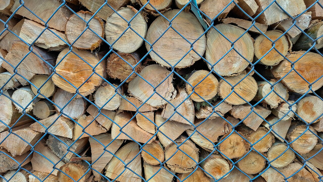 Close-up of fuelwood stored behind a protective wire mesh fence. The cross-sections of the stacked logs create a dense, natural pattern.