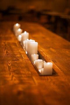 White pillar candles glow inside a long recessed channel carved through a massive timber tabletop, creating an intimate rustic centerpiece with warm light and shallow focus