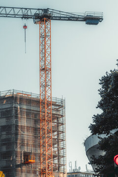 Tall orange tower crane rises above a multistory building wrapped in scaffolding and safety mesh, capturing active urban renovation and modern construction infrastructure