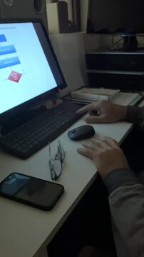 Close-up of a man's hands on a desk, as he analyzes a complex business flowchart on his computer monitor at night.