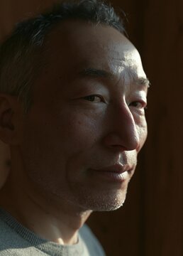 Close-up portrait of a middle-aged asian man's face. he appears to be in his late 40s or early 50s, with short, light-colored hair and a slight smile on his lips.