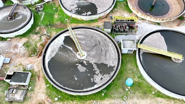 Wastewater treatment plant with circular clarifier tanks processing sewage. Urban sanitation and environmental infrastructure. Aerial drone view.