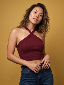 Young Asian Woman with Wavy Hair Wearing a Stylish Maroon Halter Top against Yellow Background