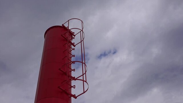 A tall red tower with metal steps under a cloudy sky.