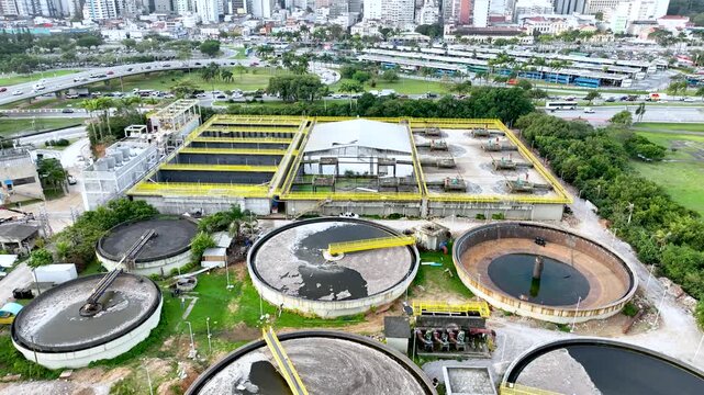 Wastewater treatment plant with circular clarifier tanks processing sewage. Urban sanitation and environmental infrastructure. Aerial drone view.