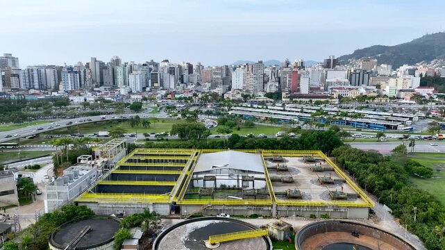 Wastewater treatment plant with circular clarifier tanks processing sewage. Urban sanitation and environmental infrastructure. Aerial drone view.