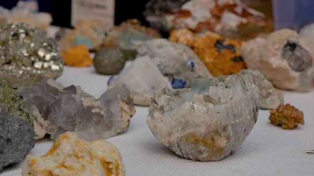 Collection of raw mineral specimens and natural crystals displayed on white cloth at a gem and mineral show. Assorted uncut natural crystals and geological rock samples with shallow depth of field.