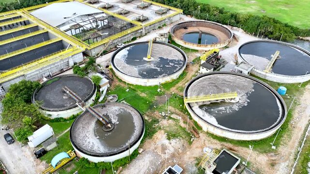Wastewater treatment plant with circular clarifier tanks processing sewage. Urban sanitation and environmental infrastructure. Aerial drone view.