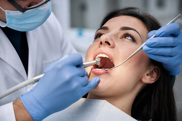 Fototapeta premium A dentist in a white coat examines a female patient's mouth with a dental mirror and probe.
