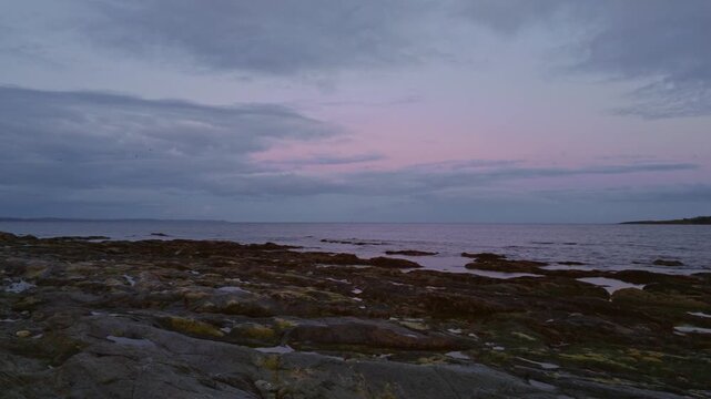 A tranquil late evening panoramic view from Hannahfore Beach near Looe in Cornwall, looking out towards the silhouette of Looe Island under a colourful sunset sky with soft clouds over the sea.