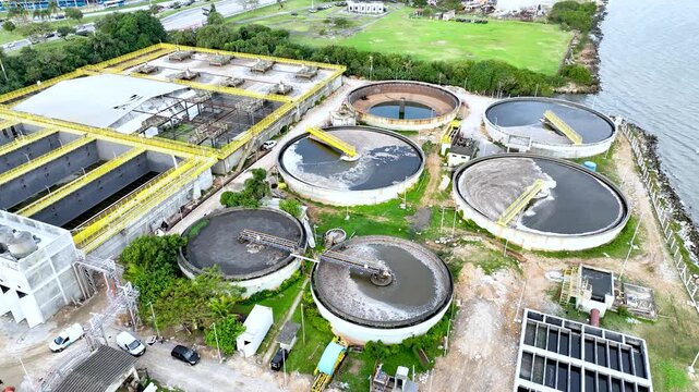 Wastewater treatment plant with circular clarifier tanks processing sewage. Urban sanitation and environmental infrastructure. Aerial drone view.