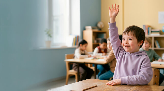 Smiling young boy with Down syndrome raising hand in classroom. Inclusive education concept with diverse students in blurred background. Copy space for text