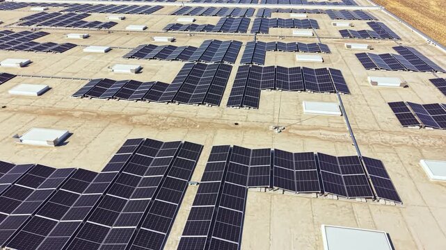 Large solar panels cover the flat roof of a building. The scene shows clear skies and fields in the background. This is a bright daytime view of renewable energy use.
