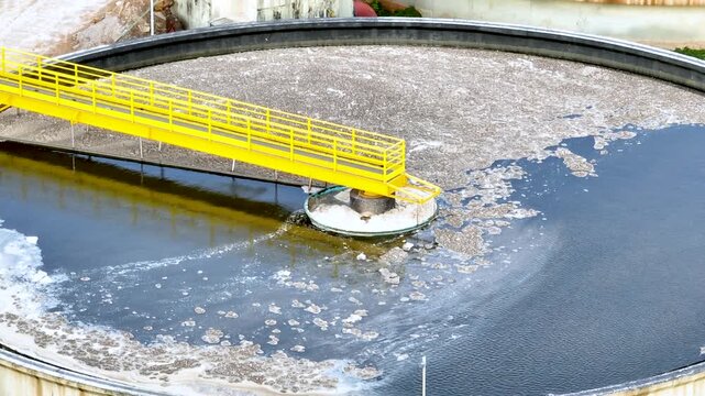 Wastewater treatment plant with circular clarifier tanks processing sewage. Urban sanitation and environmental infrastructure. Aerial drone view.