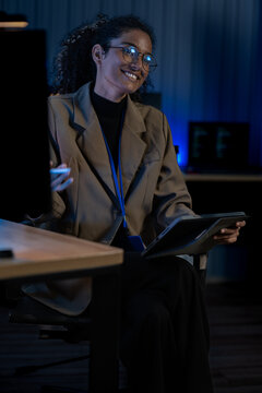 Black female IT specialist reviews server logs and network security data on monitors in a dimly lit operations room at night.