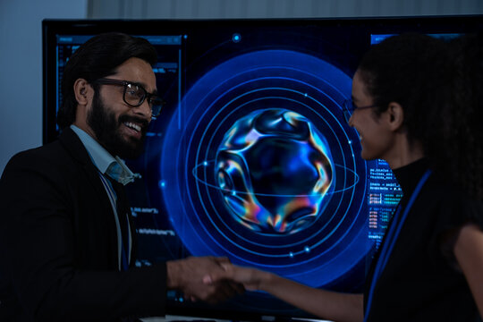 South Asian male and Black female IT analysts collaborate in front of glowing AI graphics on a large display in a dark room.