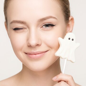 Young woman winking and holding a cute ghost lollipop for Halloween celebration