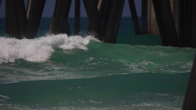 Big waves breaking under the pier at the beach
