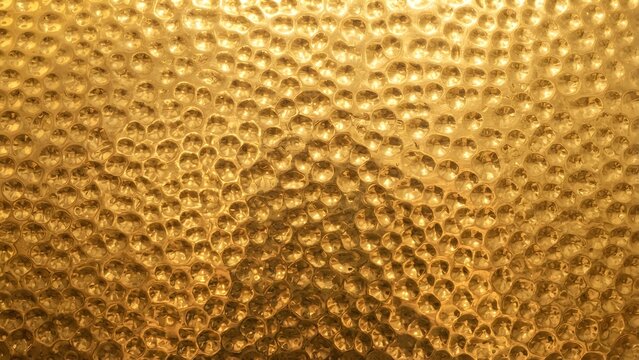 Close-up view of a hammered brass or gold textured surface with a warm, reflective glow