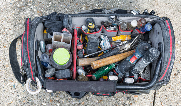 Handyman's open black tool bag illustrates construction tools on job site.