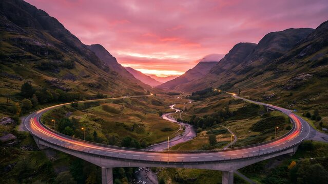 Aerial view of winding road bridge in mountain valley at sunset