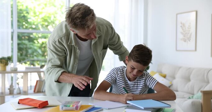 Father helping his son with homework at white table indoors