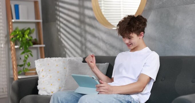 Teenager winning at video game on tablet computer on sofa in room