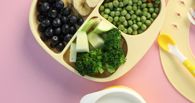 Baby dishes with foods and drink on pink table, top view. Camera moving