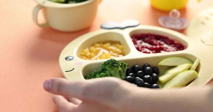 Woman placing baby dish with fresh foods on coral table, closeup