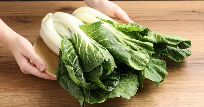 Woman putting bok choi (Chinese cabbage) on wooden table, closeup