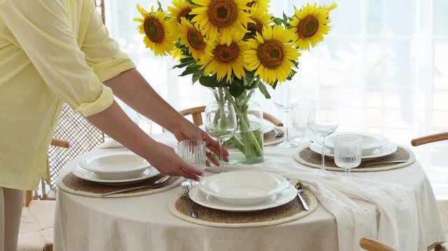 Woman setting table for dinner and beautiful sunflowers indoors, closeup