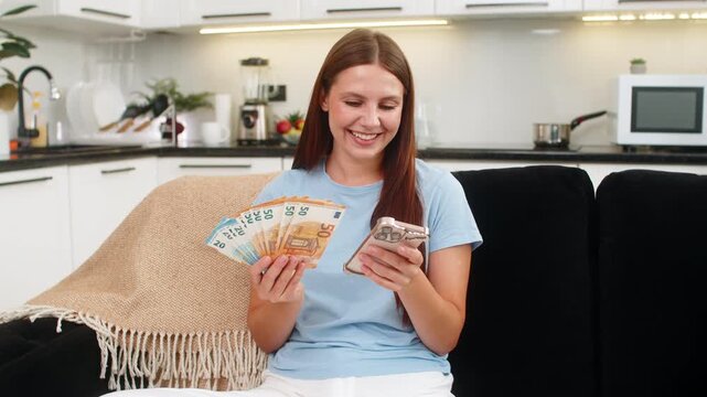 Young woman at home counts euro cash money with smartphone checks exchange rate feels proud of saving. Caucasian girl on sofa plans purchase invests savings thinks of dream buy celebrates salary bonus