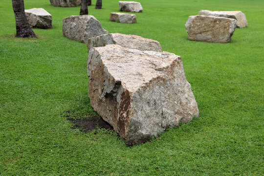 Large grey rocks boulders placed on a green lawn in a park.