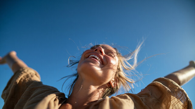 Carefree Woman Laughing with Arms Outstretched Against Blue Sky