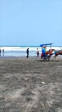 A view of people riding a decorated horse-drawn carriage on the sandy beach of Parangtritis, Yogyakarta.