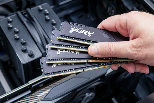 Technician holds expensive Kingston FURY DDR memory modules fanned over an open PC, with cooling equipment and graphics card visible. Astana, Kazakhstan - December 15, 2025
