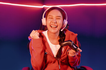 Host channel of smiling beautiful Asian girl streamer with joystick playing with raising fist up winning Esport skilled team players wearing headphones pastel media online in neon room. Stratagem. © InfiniteFlow