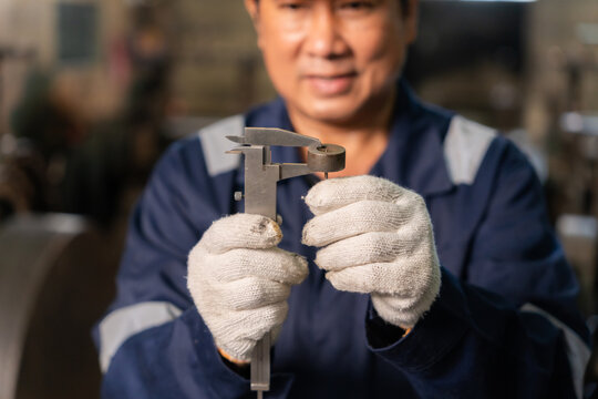 Confident technician wearing hardhat using vernier caliper to measure and inspect metal component in factory.