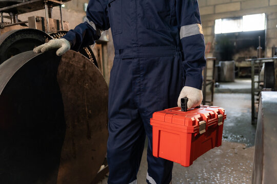 Close-up of worker hand holding orange toolbox ready for machinery maintenance in industrial factory.