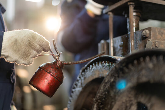 Close-up of worker hand holding oiler can to lubricate machinery gears in industrial factory.