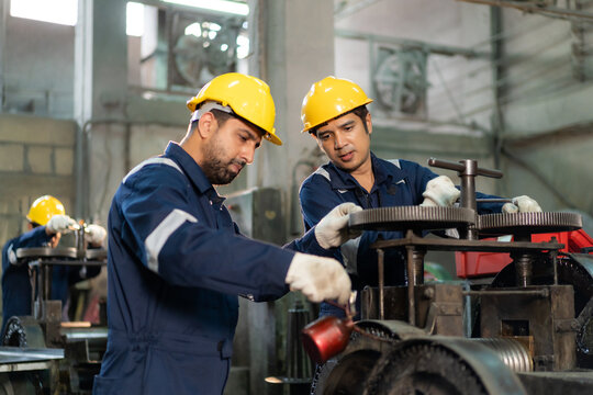 Engineers wearing hardhats working together to lubricate and repair machinery gears in industrial factory.