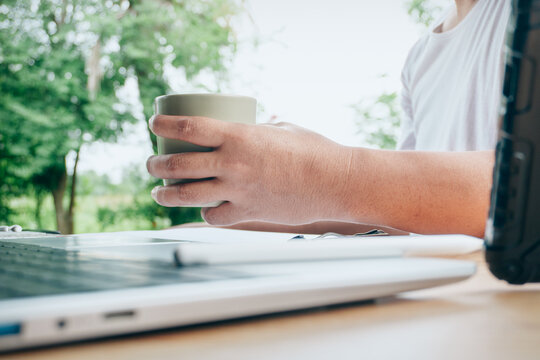 Close up of a person holding a coffee cup beside a laptop in a bright home workspace, representing remote work, morning routine, productivity, coffee break, technology and a relaxed lifestyle