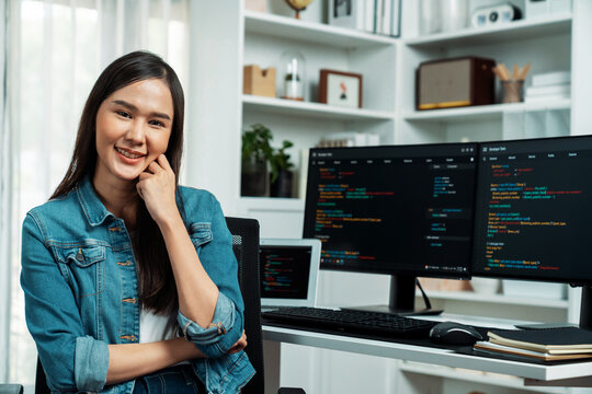 Young Asian in IT developer looking at camera to present with online information on pc with coding program data application, wearing jeans shirt. surround by safety analysis two screens. Stratagem.