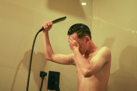 Man Holding Hand Shower and Rinsing His face in Warm Tiled Bathroom