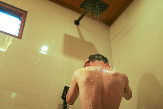 Back View of Young Asian Man Standing Under Falling Water in Modern Rain Shower