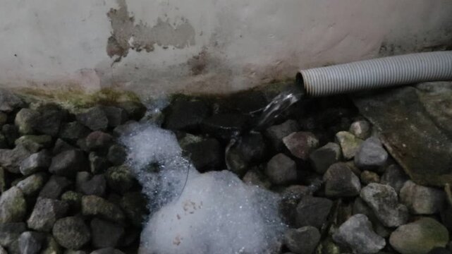 Household wastewater from washing activities flowing out through a drainage channel in an urban area, illustrating graywater discharge, drainage infrastructure, and urban environmental issues.