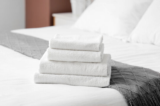 Hotel luxury and comfort, stack of clean white towels on a freshly made bed in a modern bedroom interior